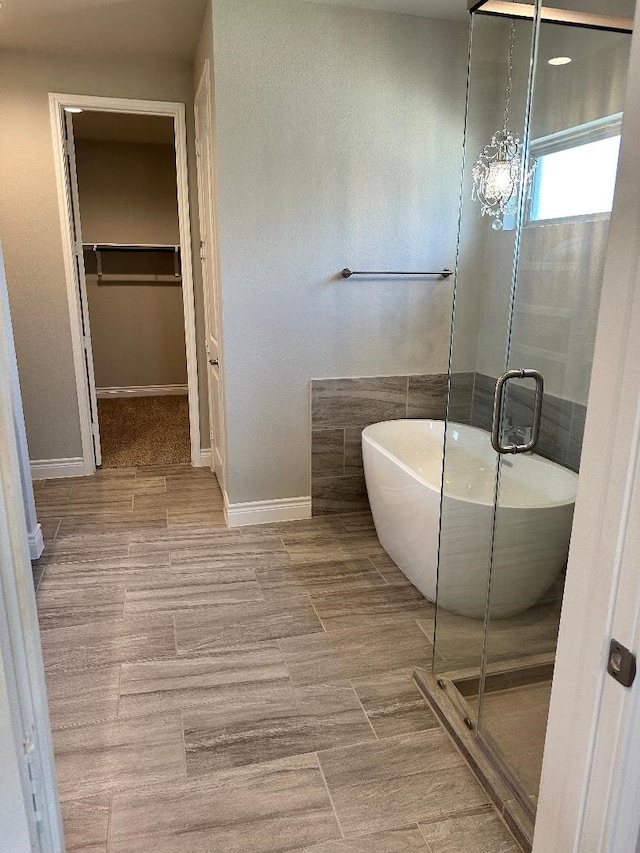 full bathroom featuring a walk in closet, wood finished floors, a freestanding bath, and a stall shower