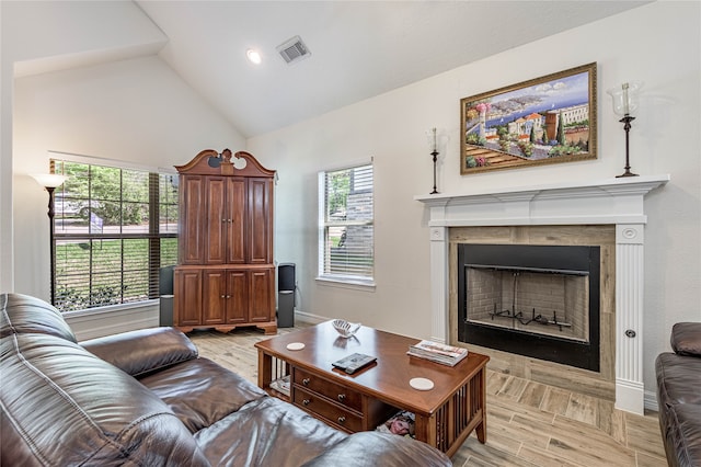 living room with light wood-type flooring, a tiled fireplace, and high vaulted ceiling