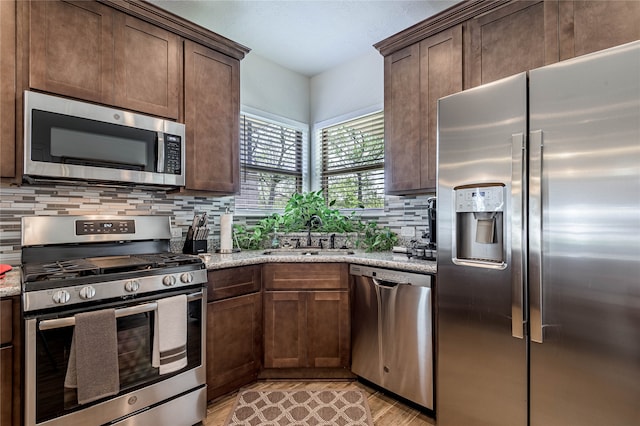 kitchen with light stone countertops, light hardwood / wood-style floors, appliances with stainless steel finishes, and sink