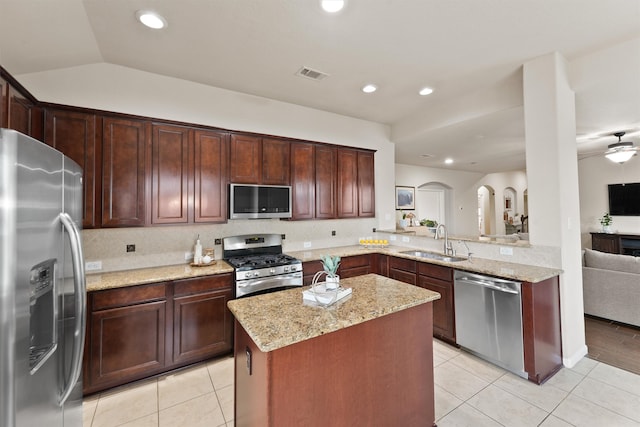 kitchen with light stone counters, sink, kitchen peninsula, appliances with stainless steel finishes, and a center island