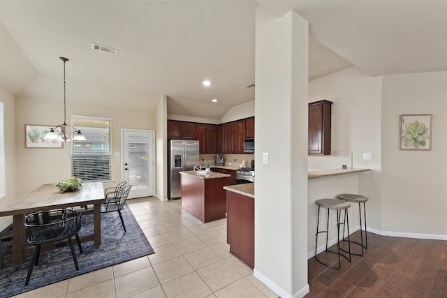 kitchen featuring lofted ceiling, kitchen peninsula, decorative light fixtures, stainless steel appliances, and light wood-type flooring