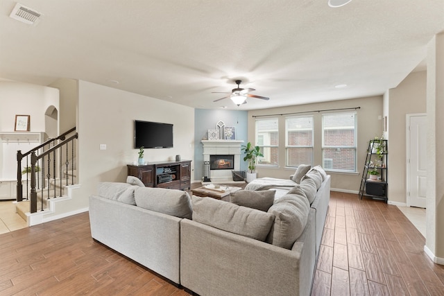 living room with light wood-type flooring, ceiling fan, and a textured ceiling