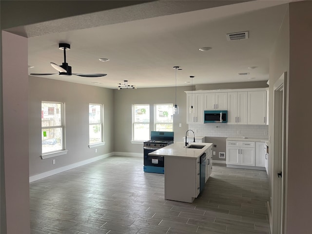 kitchen with appliances with stainless steel finishes, ceiling fan, sink, a center island with sink, and white cabinets