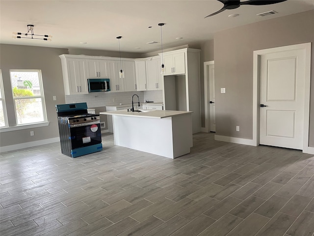 kitchen featuring hanging light fixtures, light hardwood / wood-style flooring, an island with sink, appliances with stainless steel finishes, and white cabinetry