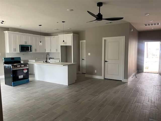 kitchen with backsplash, an island with sink, white cabinetry, wood-type flooring, and stainless steel appliances