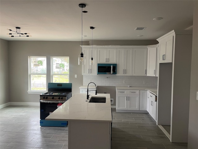 kitchen featuring black gas range, sink, light stone countertops, an island with sink, and white cabinetry