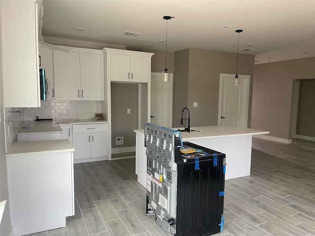 kitchen with sink, light hardwood / wood-style flooring, an island with sink, decorative light fixtures, and white cabinetry