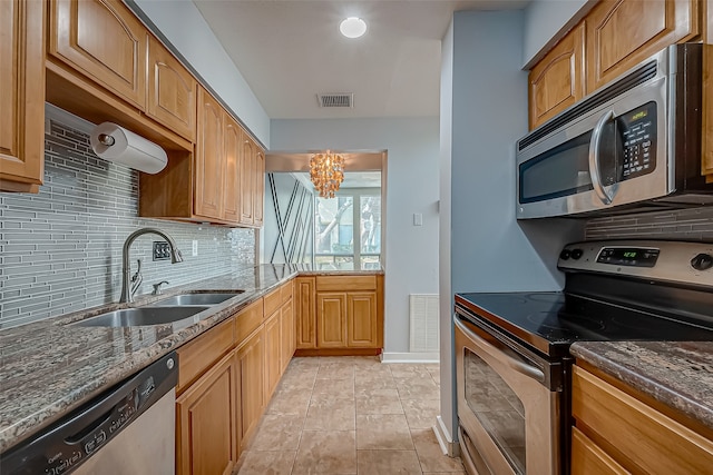 kitchen with appliances with stainless steel finishes, sink, dark stone countertops, decorative backsplash, and a chandelier