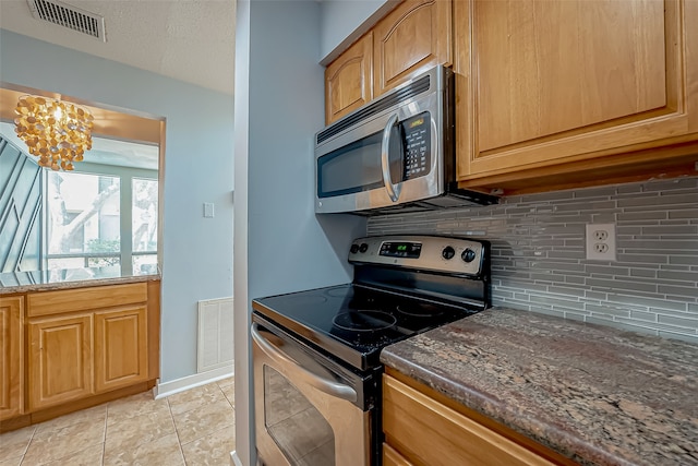 kitchen with tasteful backsplash, appliances with stainless steel finishes, dark stone counters, light tile patterned flooring, and a notable chandelier