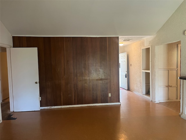 unfurnished room with built in shelves and wooden walls