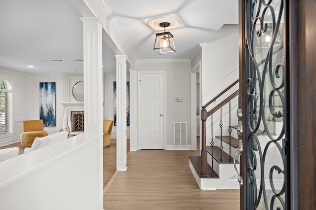 foyer entrance featuring ornamental molding, decorative columns, and light wood-type flooring