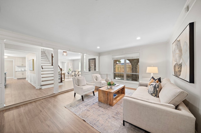 living room with light wood-type flooring, crown molding, and decorative columns