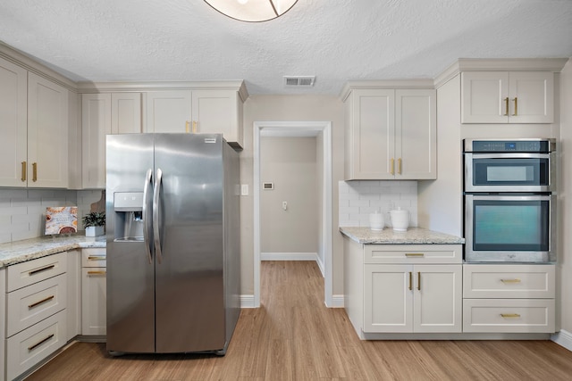 kitchen with stainless steel appliances, light hardwood / wood-style floors, tasteful backsplash, and light stone counters