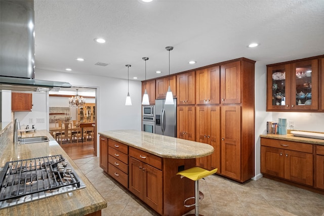 kitchen featuring range hood, decorative light fixtures, sink, light stone counters, and stainless steel appliances