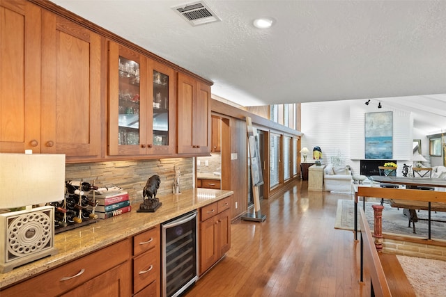 kitchen featuring light stone counters, lofted ceiling, beverage cooler, backsplash, and hardwood / wood-style floors