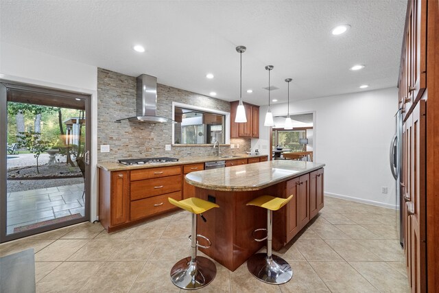 kitchen with wall chimney range hood, a kitchen island, decorative light fixtures, stainless steel appliances, and a kitchen bar