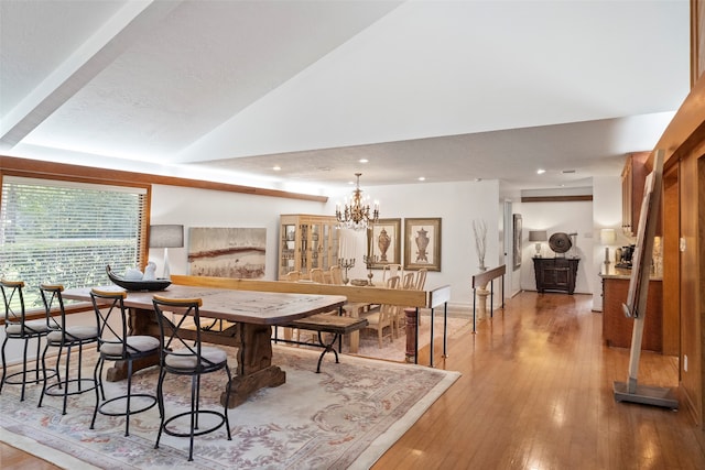 dining area with wood-type flooring, vaulted ceiling, and a chandelier