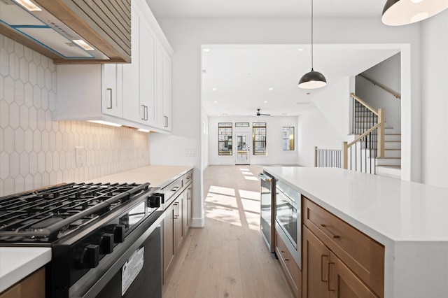 kitchen featuring exhaust hood, backsplash, hanging light fixtures, stainless steel appliances, and white cabinets