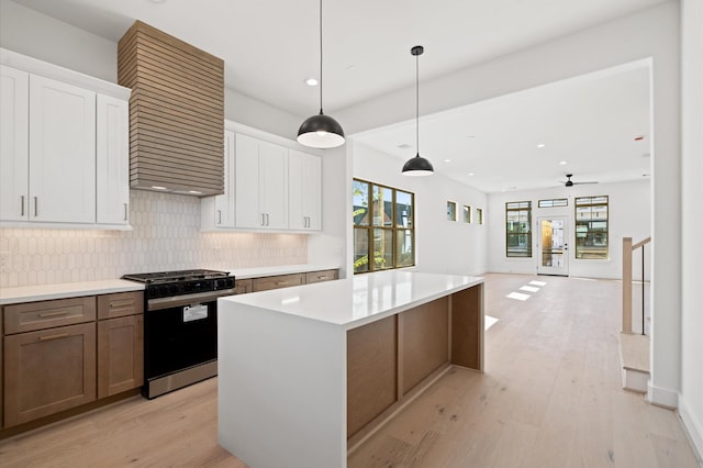 kitchen featuring white cabinetry, ceiling fan, gas range, a kitchen island, and pendant lighting