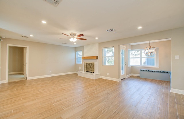 unfurnished living room featuring a large fireplace, ceiling fan with notable chandelier, and light hardwood / wood-style floors