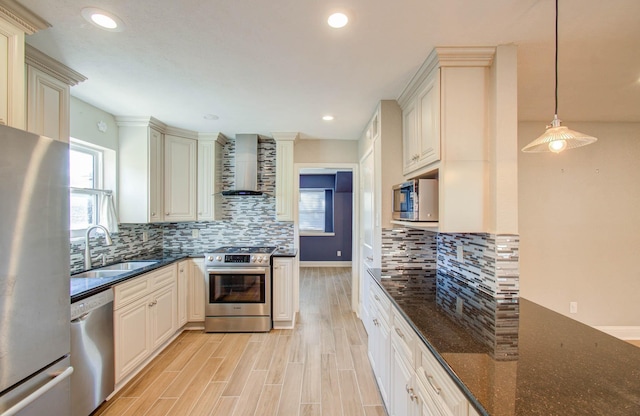 kitchen featuring sink, stainless steel appliances, wall chimney range hood, dark stone countertops, and pendant lighting