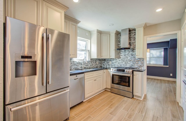 kitchen with a wealth of natural light, sink, wall chimney range hood, cream cabinets, and appliances with stainless steel finishes