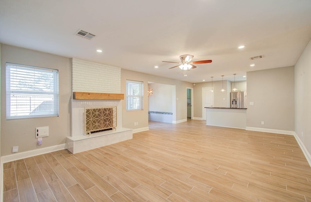 unfurnished living room featuring a large fireplace, light hardwood / wood-style floors, and ceiling fan