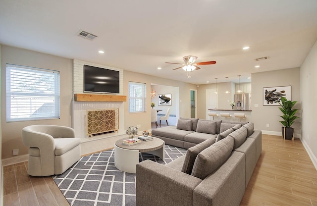 living room featuring a fireplace, light hardwood / wood-style floors, and ceiling fan