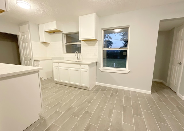 kitchen with tasteful backsplash, white cabinetry, a textured ceiling, light hardwood / wood-style floors, and sink