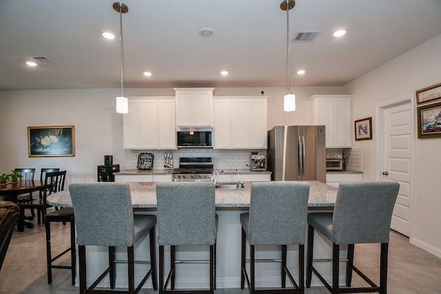 kitchen featuring stainless steel appliances, visible vents, white cabinets, decorative backsplash, and an island with sink