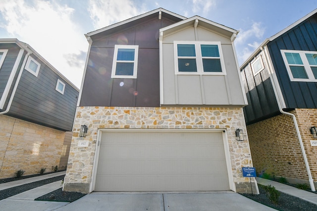 view of front of house with driveway, stone siding, a garage, and board and batten siding