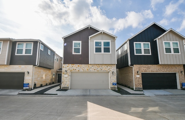 multi unit property featuring an attached garage, stone siding, driveway, and board and batten siding