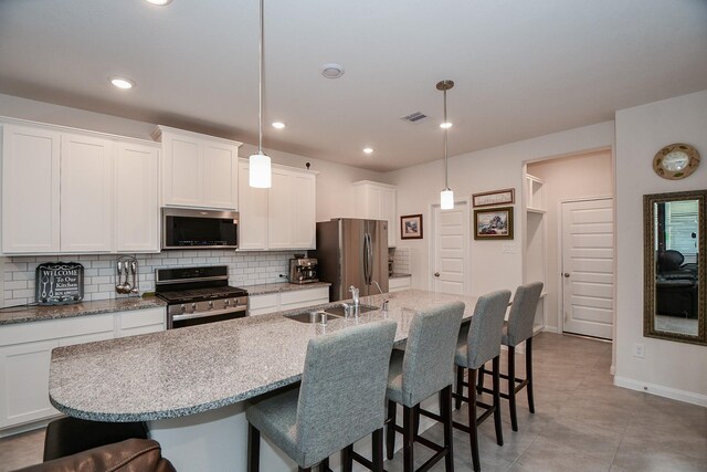 kitchen featuring an island with sink, sink, hanging light fixtures, white cabinetry, and appliances with stainless steel finishes