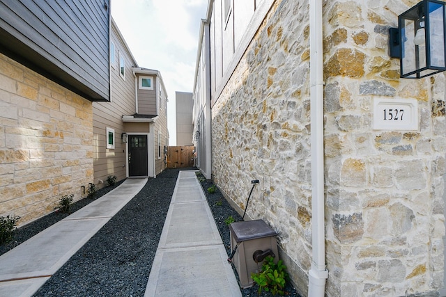 view of side of home with stone siding and fence