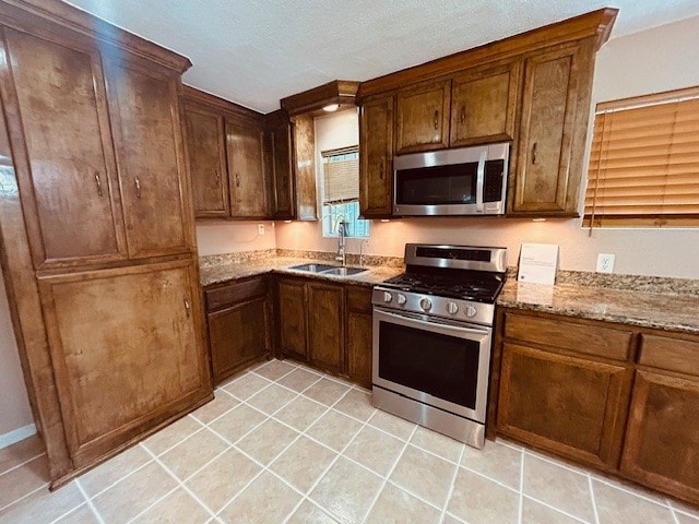 kitchen with light stone counters, stainless steel appliances, sink, light tile patterned flooring, and a textured ceiling