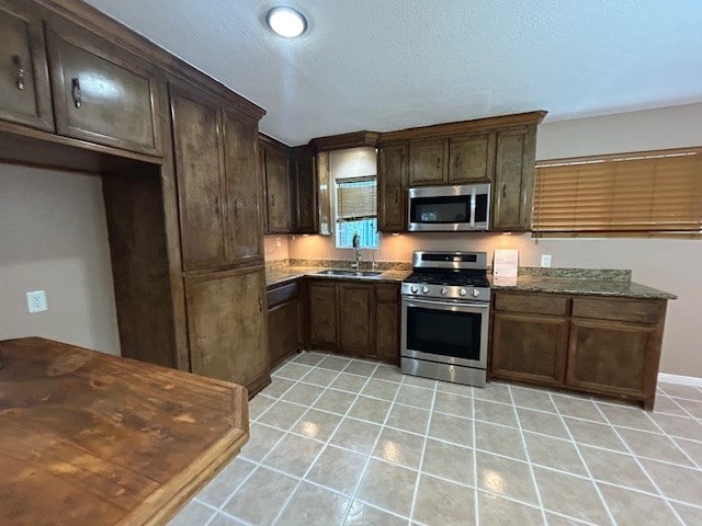 kitchen featuring dark stone countertops, dark brown cabinets, stainless steel appliances, and sink