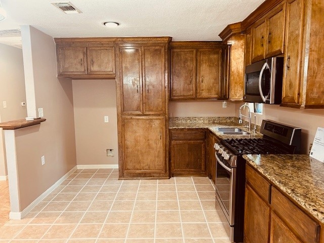 kitchen with light tile patterned floors, light stone countertops, appliances with stainless steel finishes, and sink