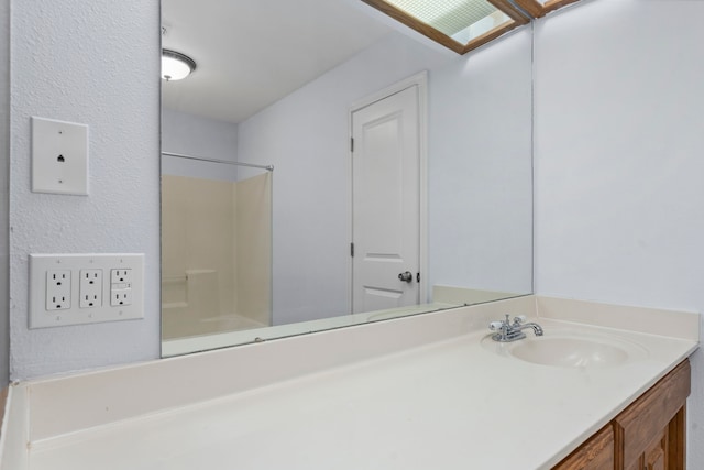 bathroom featuring vanity, a skylight, and a shower