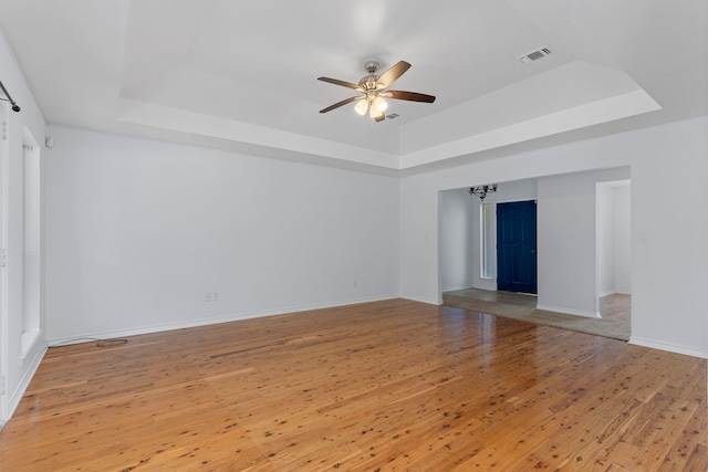 unfurnished living room featuring a raised ceiling, wood-type flooring, and ceiling fan