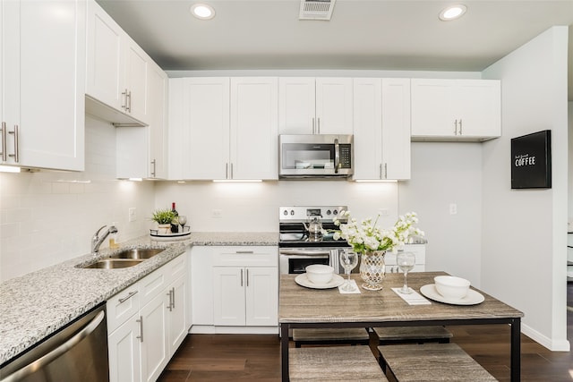 kitchen with light stone counters, white cabinets, appliances with stainless steel finishes, and dark hardwood / wood-style flooring