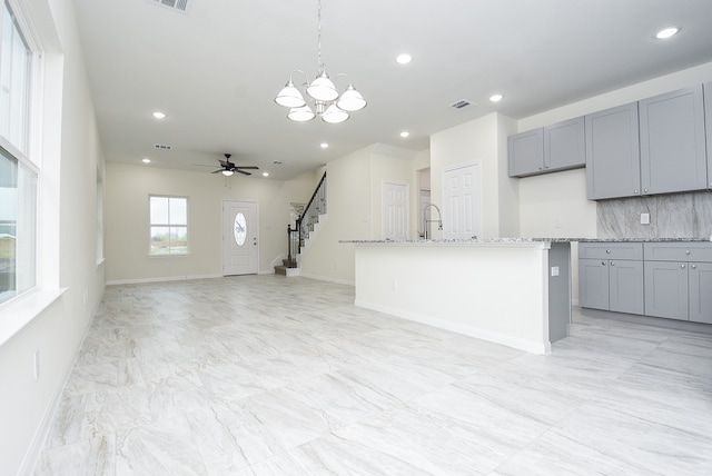 kitchen with light stone counters, pendant lighting, gray cabinets, and a center island with sink