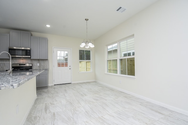 kitchen featuring stainless steel appliances, tasteful backsplash, a chandelier, and gray cabinetry