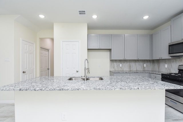 kitchen with a kitchen island with sink, gray cabinetry, sink, backsplash, and appliances with stainless steel finishes