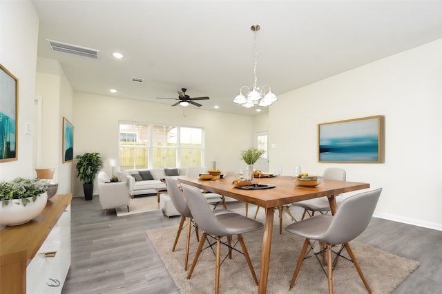 dining space featuring wood-type flooring and ceiling fan with notable chandelier