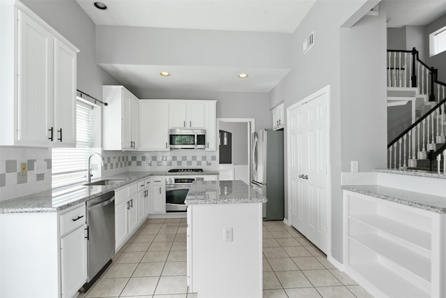 kitchen with white cabinets, stainless steel appliances, light stone counters, and sink