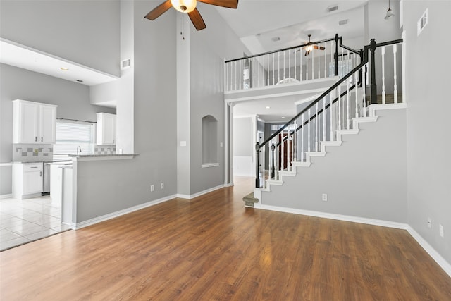 unfurnished living room with ceiling fan, light wood-type flooring, and a high ceiling