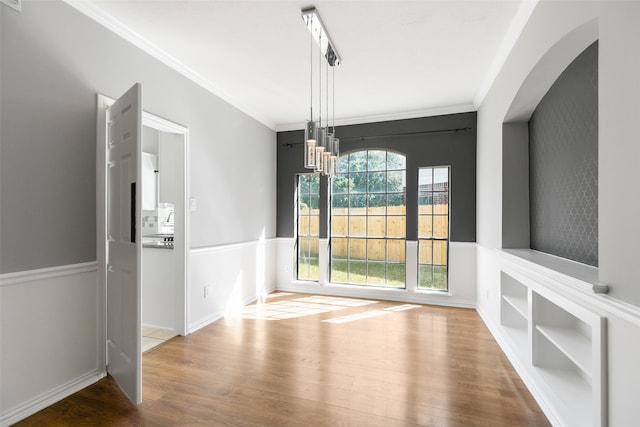 unfurnished dining area featuring wood-type flooring, crown molding, and a chandelier