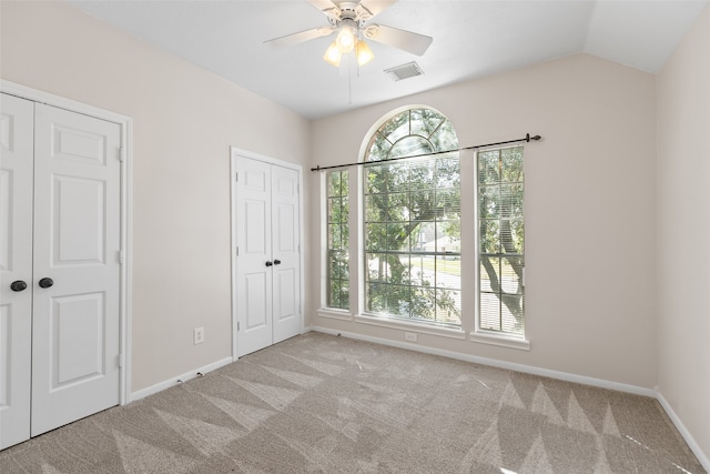 unfurnished bedroom with multiple windows, light carpet, ceiling fan, and two closets