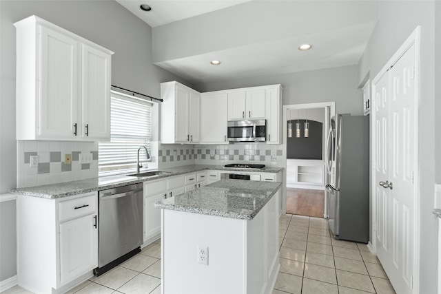 kitchen with light stone countertops, appliances with stainless steel finishes, sink, white cabinets, and a kitchen island