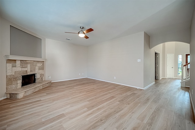 unfurnished living room featuring ceiling fan, a stone fireplace, and light hardwood / wood-style flooring